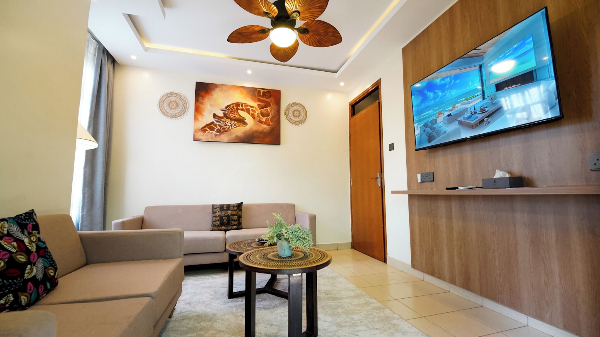 A modern living room with a sofa, a coffee table, a television mounted on a wooden wall, and a ceiling fan.