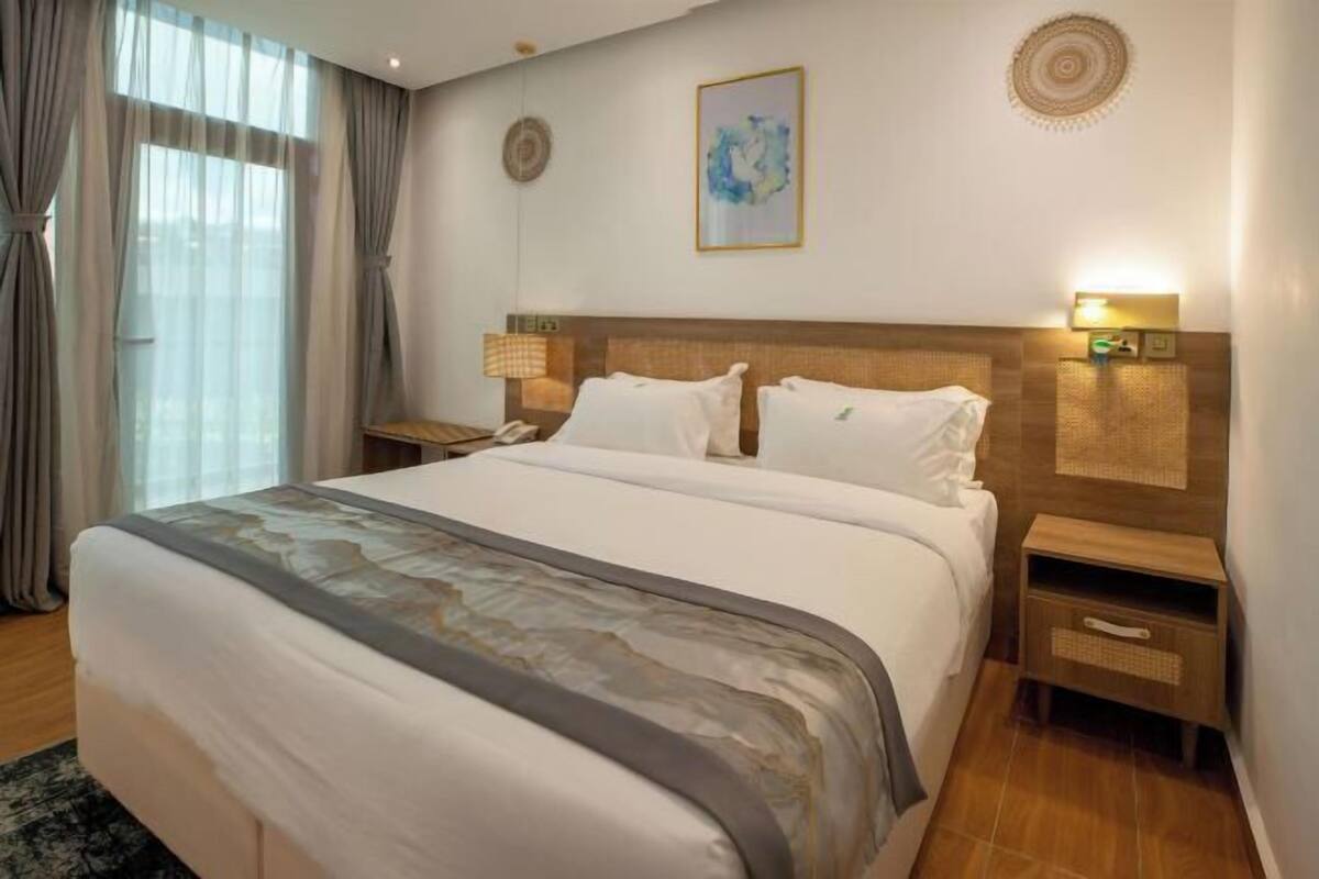 A hotel room with a large bed, a bedside table with a lamp, a wall-mounted artwork, and a nightstand with a phone.