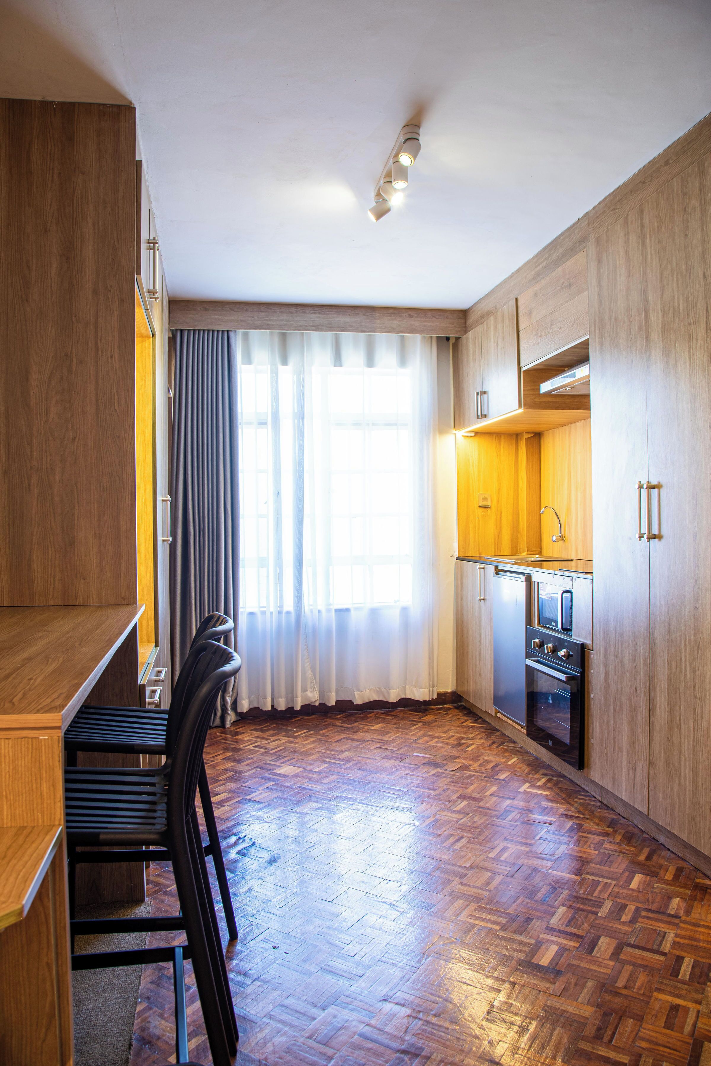 A compact kitchen with wooden cabinets, a built-in oven, and a dining area with chairs.