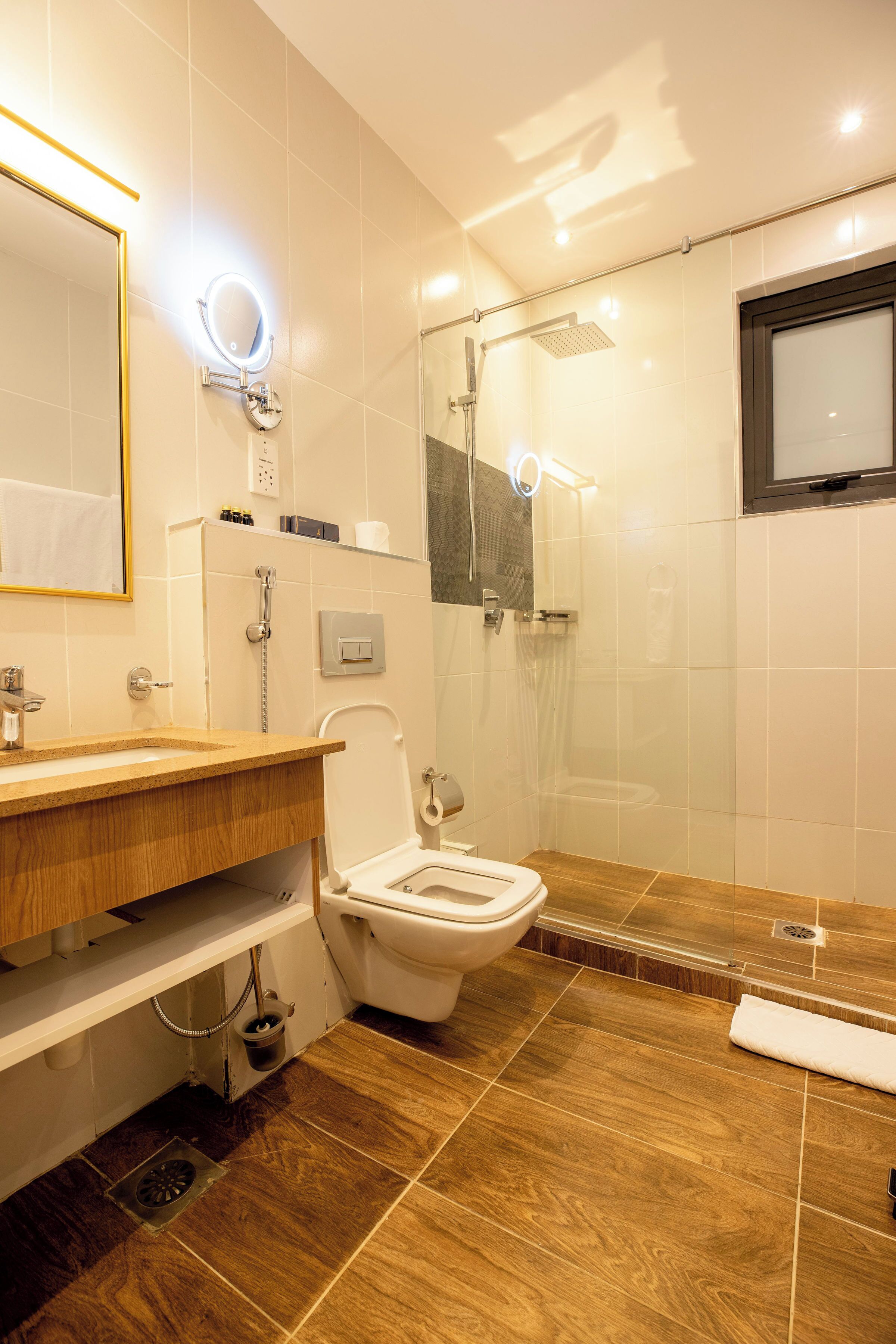 A modern bathroom with a wooden vanity, a toilet, a shower with a glass enclosure, and a mirror with a light.