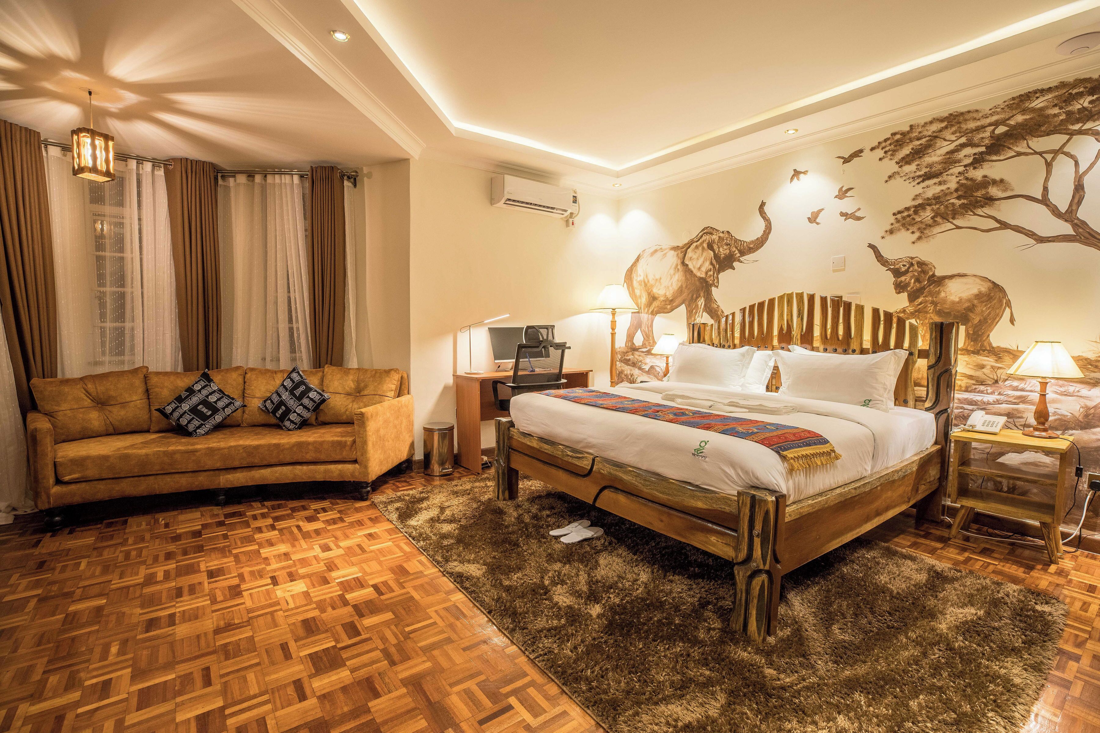 A hotel room with a wooden floor, a bed with a headboard, a sofa, a desk, and a wall mural.