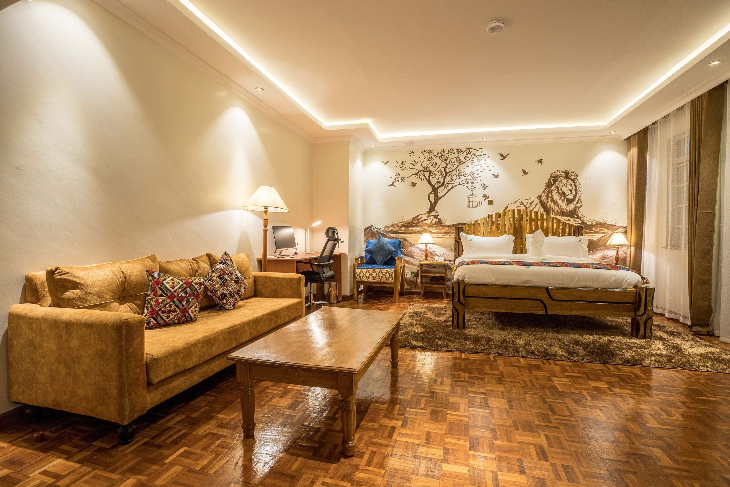 A hotel room with a wooden floor, a sofa, a bed, a desk, and a wall mural.