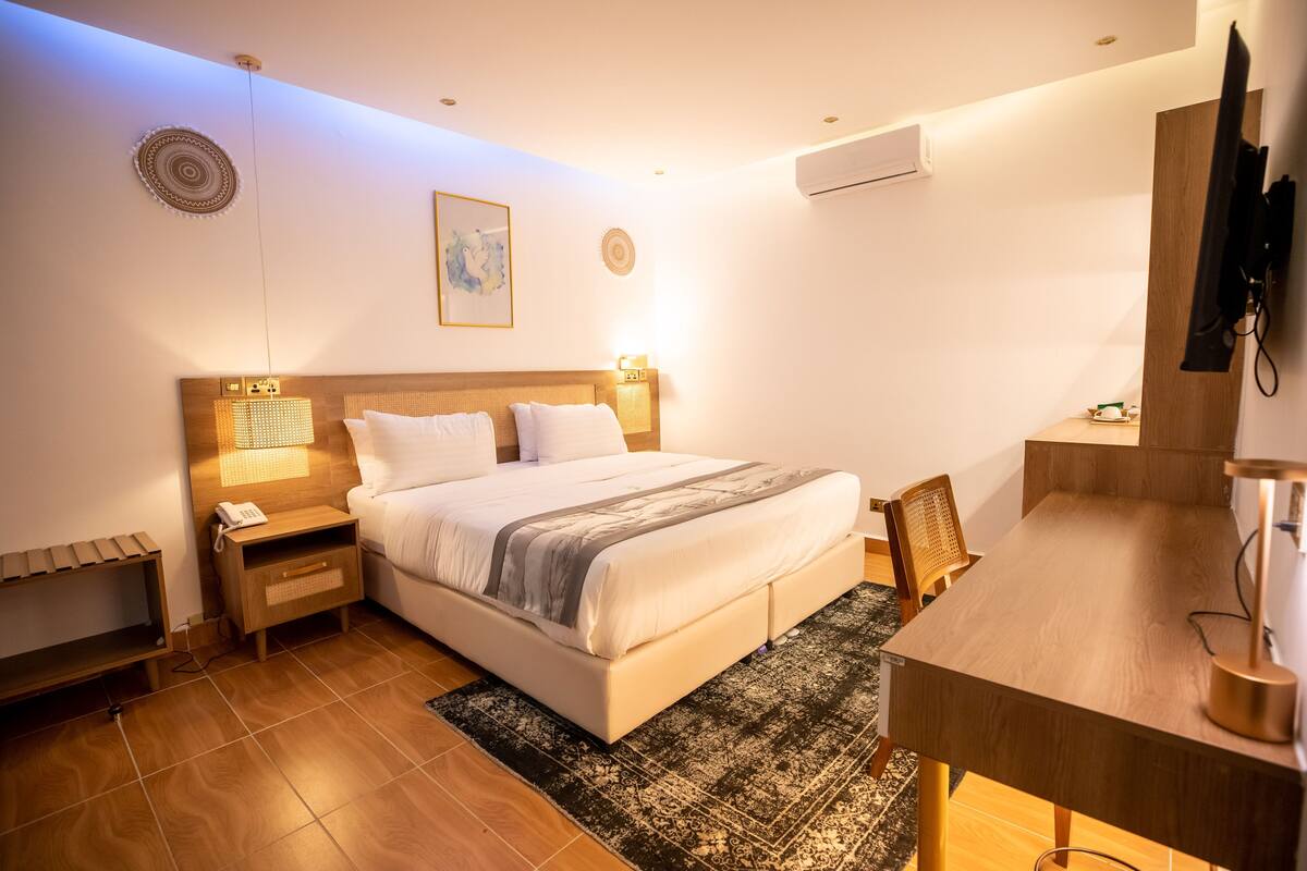 A hotel room with a bed, bedside table, desk, chair, and a television mounted on the wall.