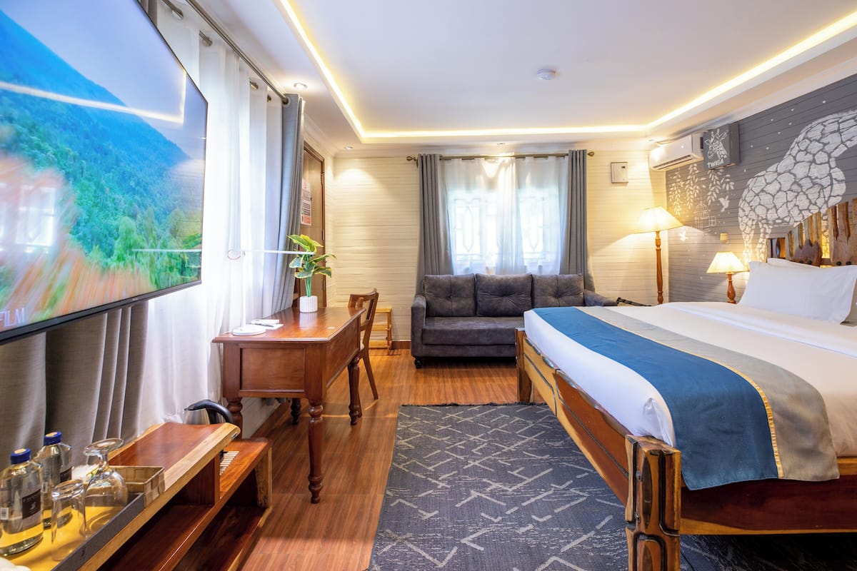 A hotel room with a bed, a sofa, a desk, a TV, and a window with curtains.