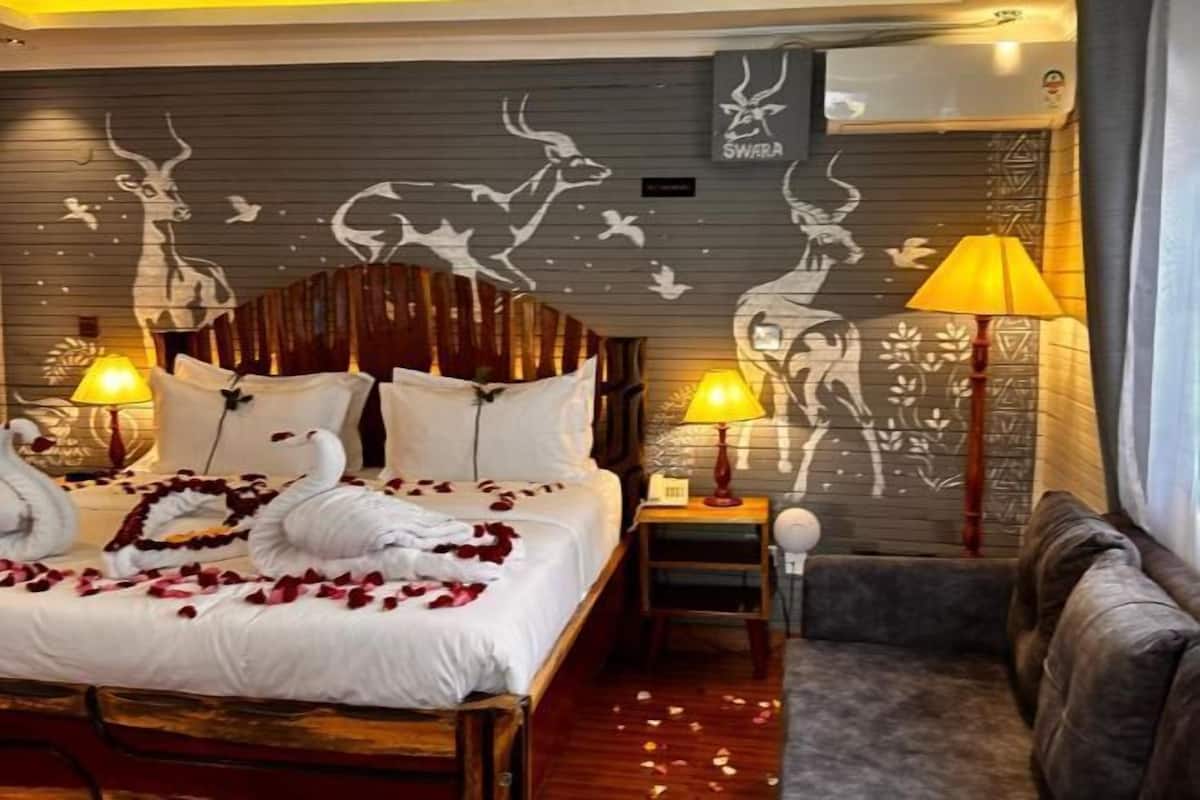 A hotel room with a bed, two bedside lamps, a nightstand, a sofa, and wall art featuring animal silhouettes.