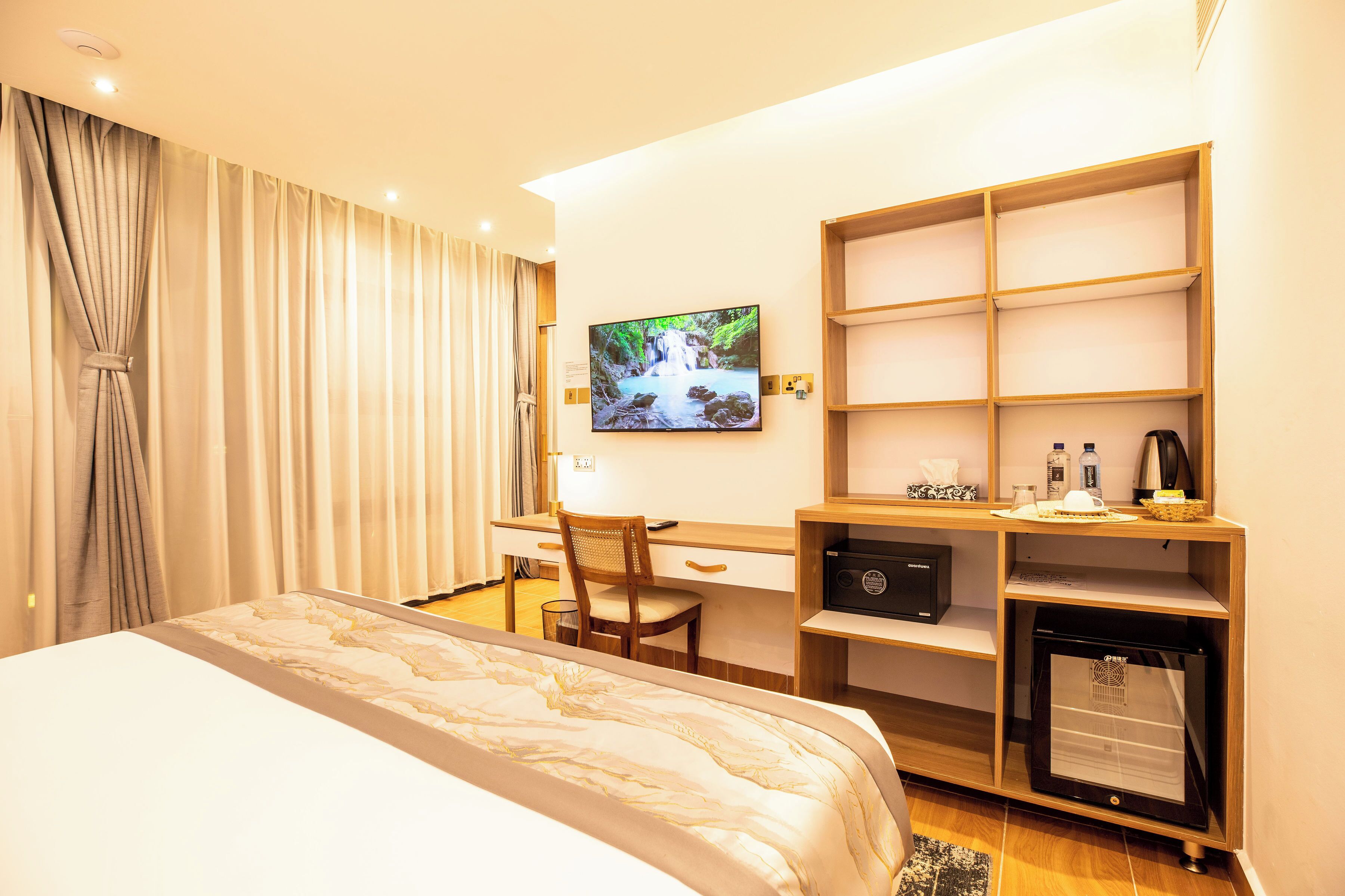 A hotel room with a bed, desk, chair, TV, and a small refrigerator.