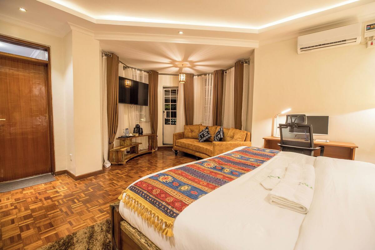 A hotel room with a large bed, a sofa, a TV, and a desk with a computer.