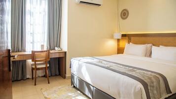 A hotel room with a bed, desk, chair, and an air conditioning unit.