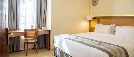 A hotel room with a bed, desk, chair, and an air conditioning unit.