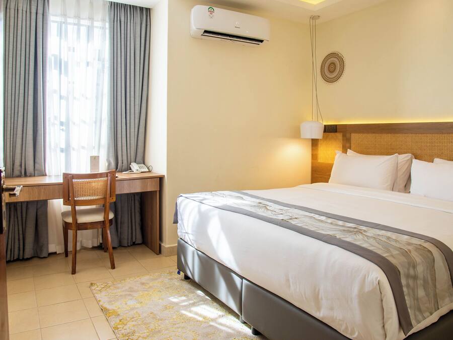 A hotel room with a bed, desk, chair, and an air conditioning unit.