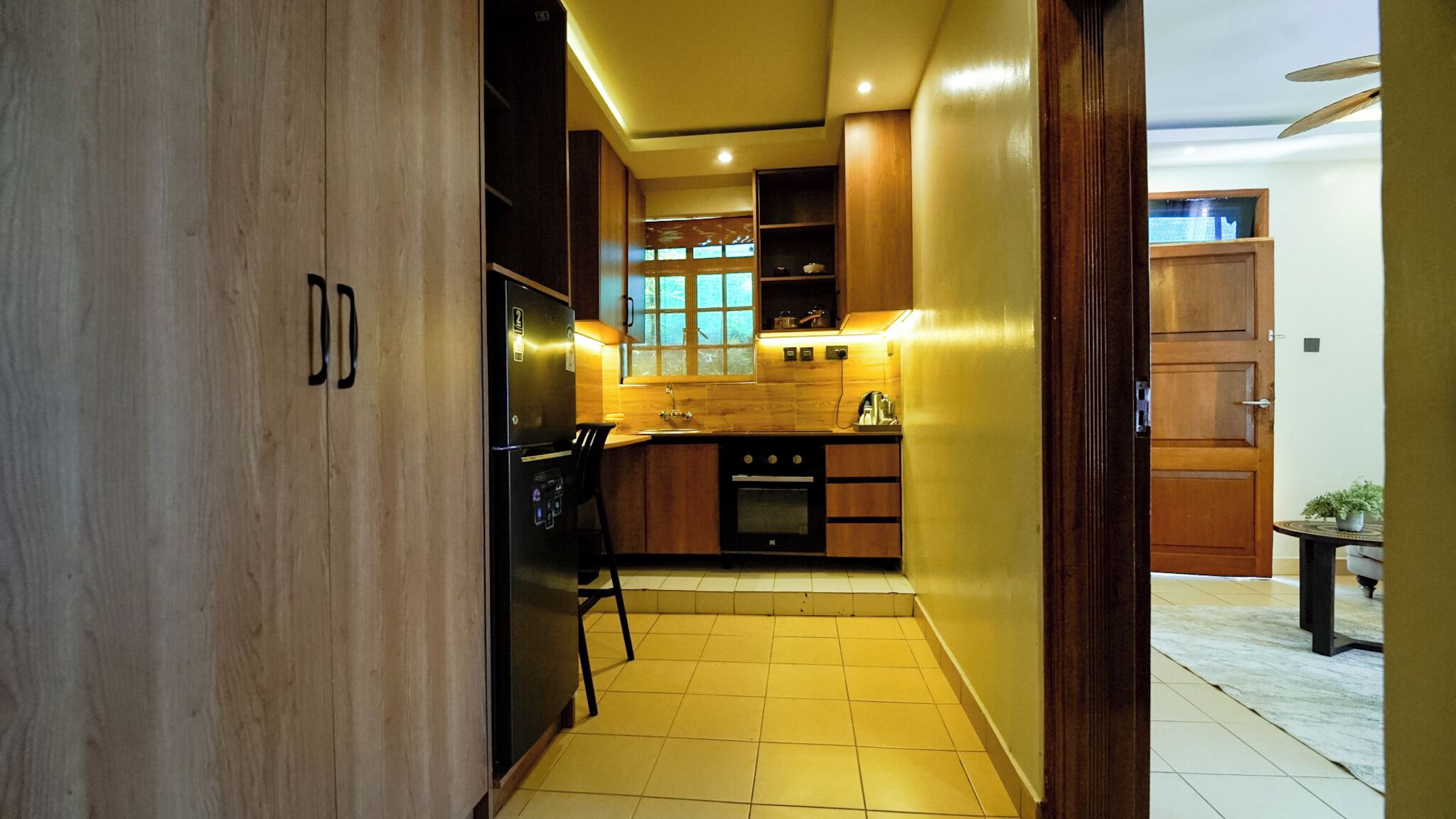 Une cuisine moderne avec des meubles en bois, un réfrigérateur noir et un sol carrelé.