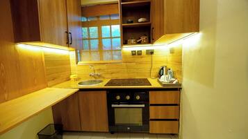 A compact kitchen with wooden cabinets, a built-in oven, a sink, and a window with blinds.