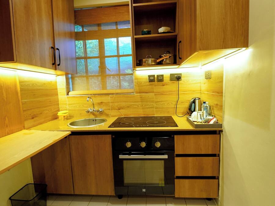 A compact kitchen with wooden cabinets, a built-in oven, a sink, and a window with blinds.