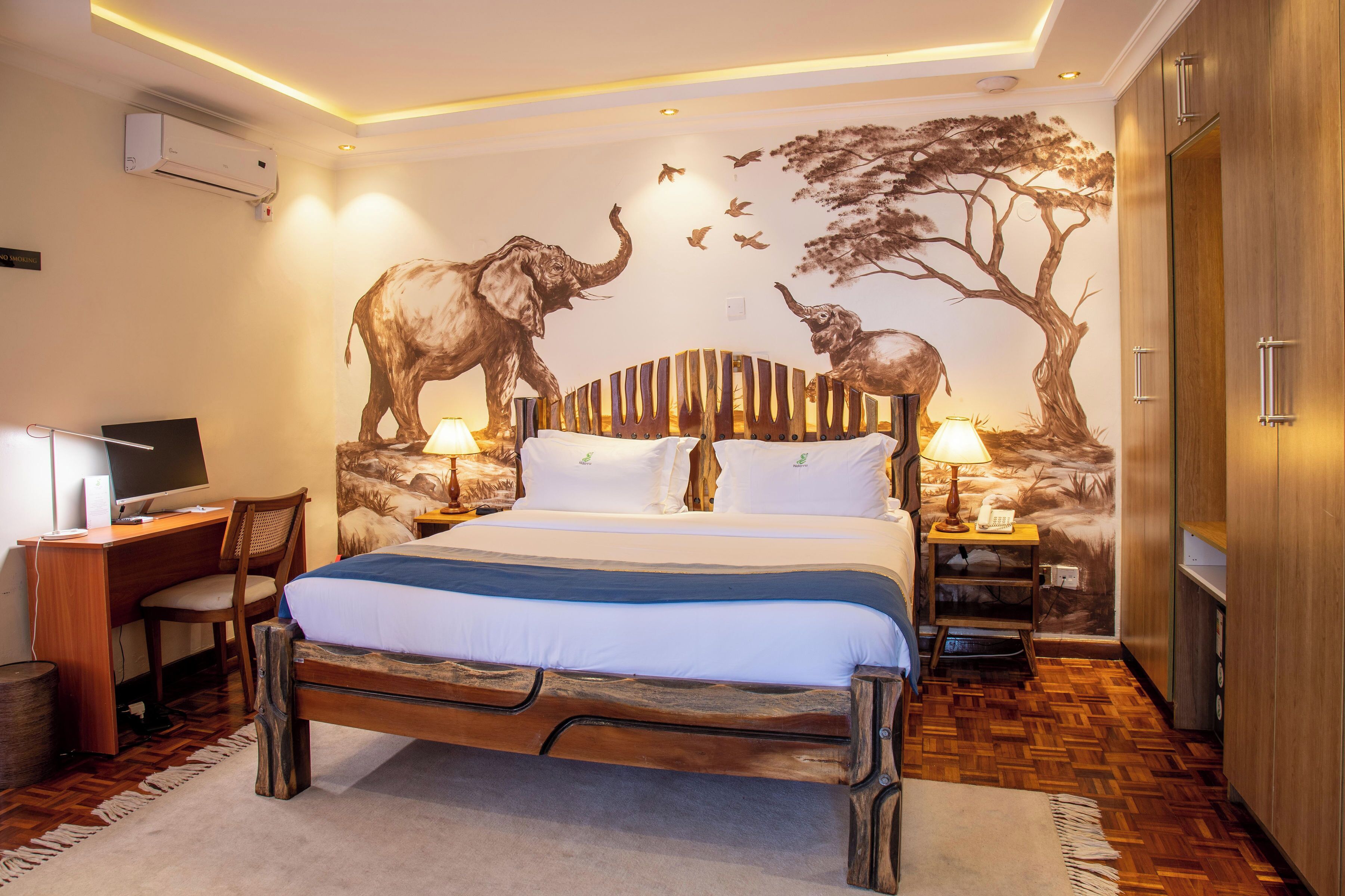 A bedroom with a bed, desk, chair, and wall art depicting elephants and birds.
