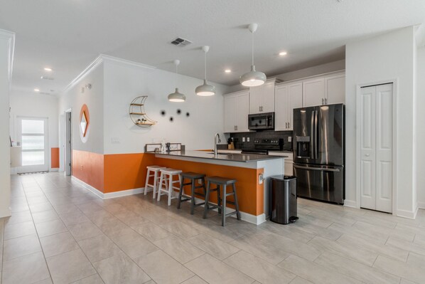 A modern kitchen with white cabinets, a stainless steel refrigerator, a microwave, and a bar area with stools.