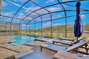 A covered outdoor pool area with lounge chairs and a hot tub, surrounded by a greenhouse structure. - 9 Bedroom waterfront pool home in Storey Lake Resort (Kissimmee)