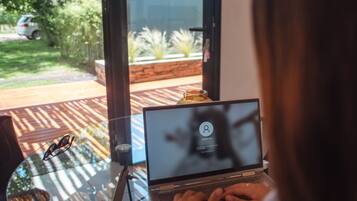 A laptop on a glass table with a view of a garden and a parked car outside.