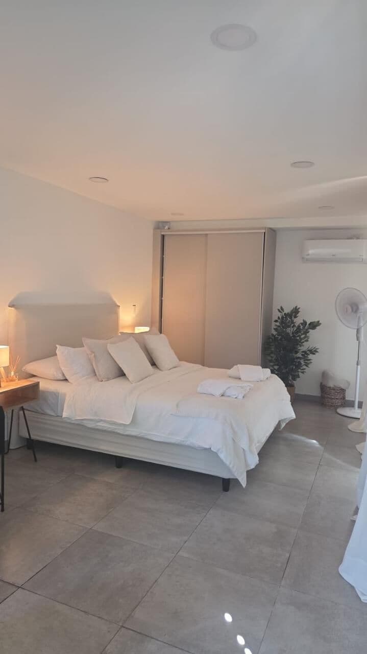 A modern bedroom with a bed, bedside tables, a floor lamp, and a potted plant.