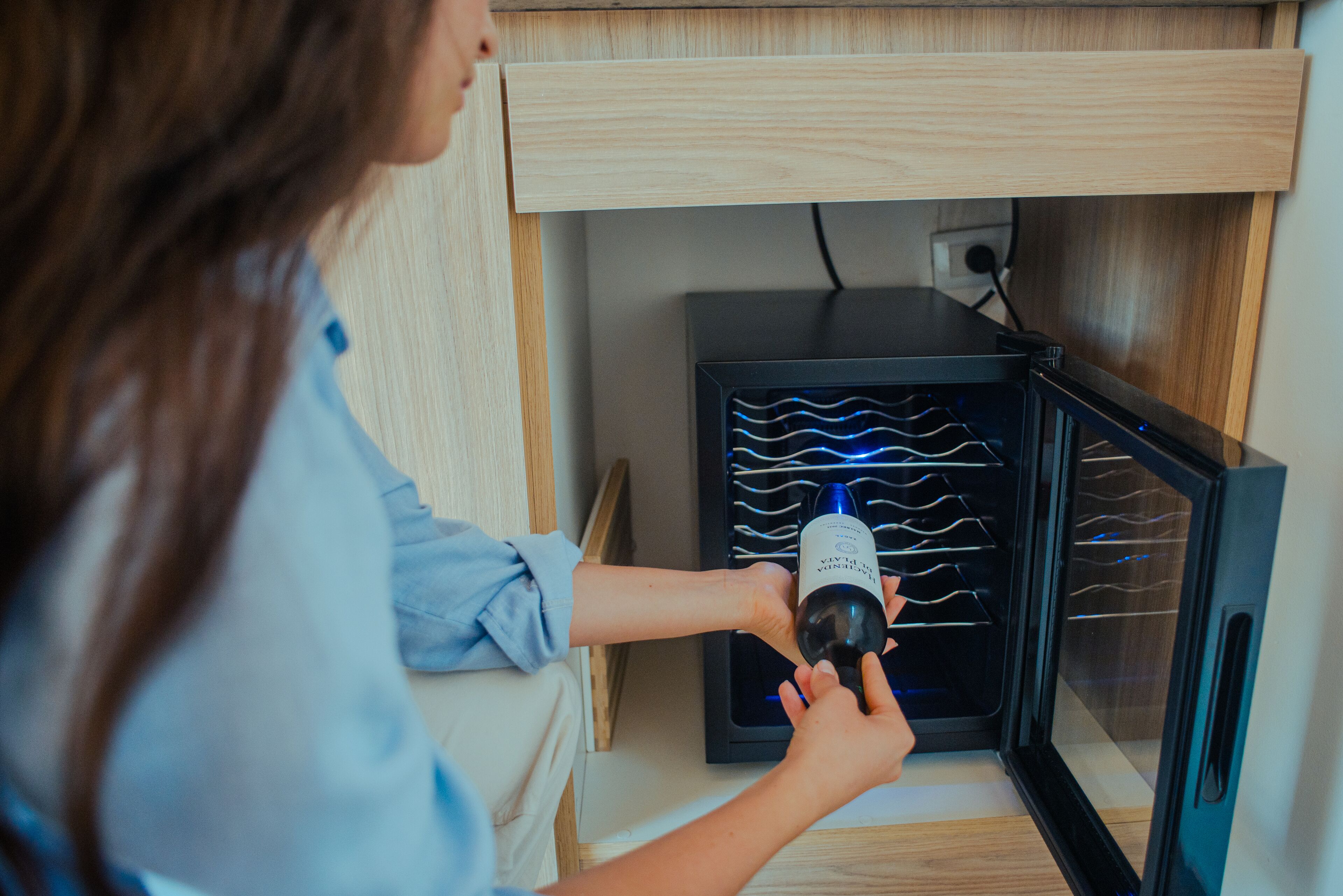 A person placing a wine bottle into a wine cooler with a built-in wine rack.