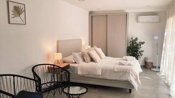A modern hotel room with a bed, bedside table, lamp, chairs, and a potted plant.