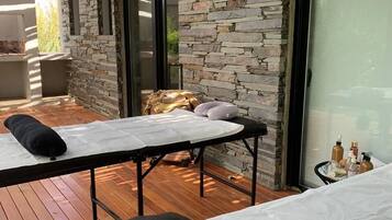 A spa area with wooden flooring, stone walls, and two massage tables with towels and pillows.