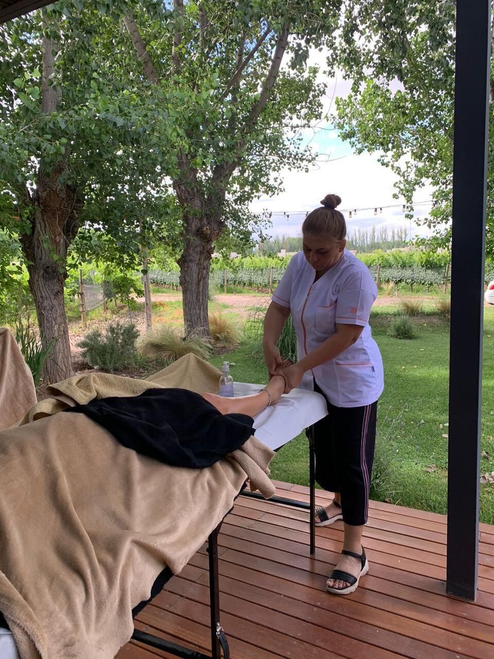 A person performing a massage on another individual seated on a wooden deck.