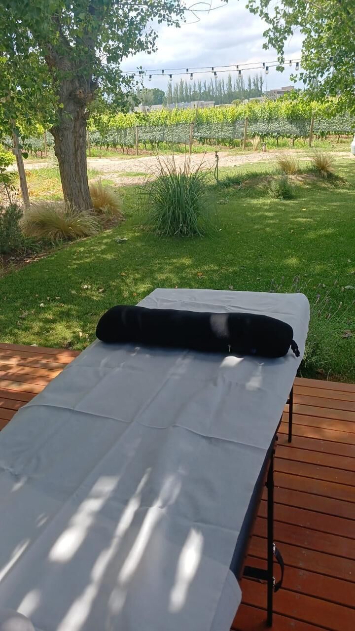 Een massagetafel met een zwart kussen op een houten terras, met uitzicht op een wijngaard.