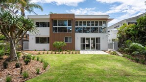 A modern two-story house with a flat roof, large windows, and a wooden accent wall. - Coastal Escape – waterfront reserve on Jervis Bay (Vincentia)