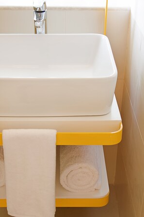 A bathroom with a white bathtub, a yellow shelf, and two rolled towels.