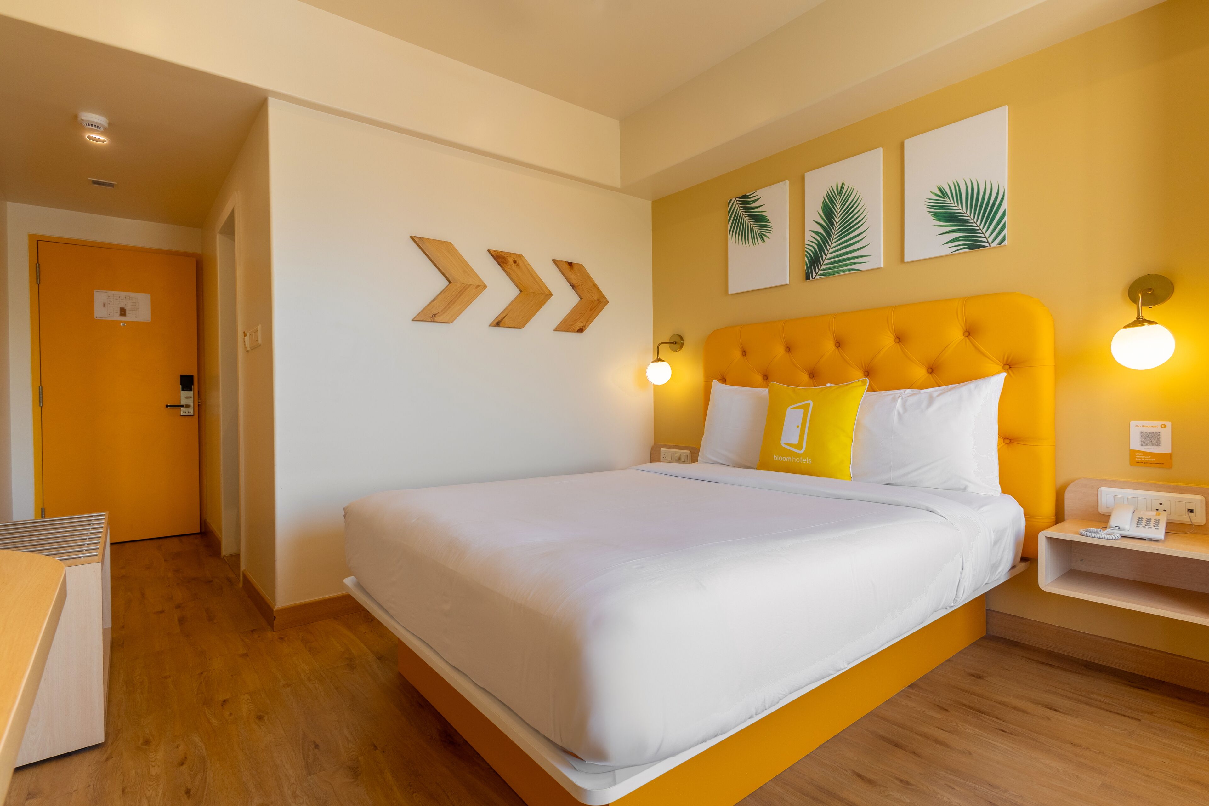 A hotel room with a large bed, a yellow headboard, and a bedside table with a phone.