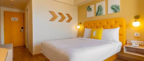 A hotel room with a large bed, a yellow headboard, and a bedside table with a phone.