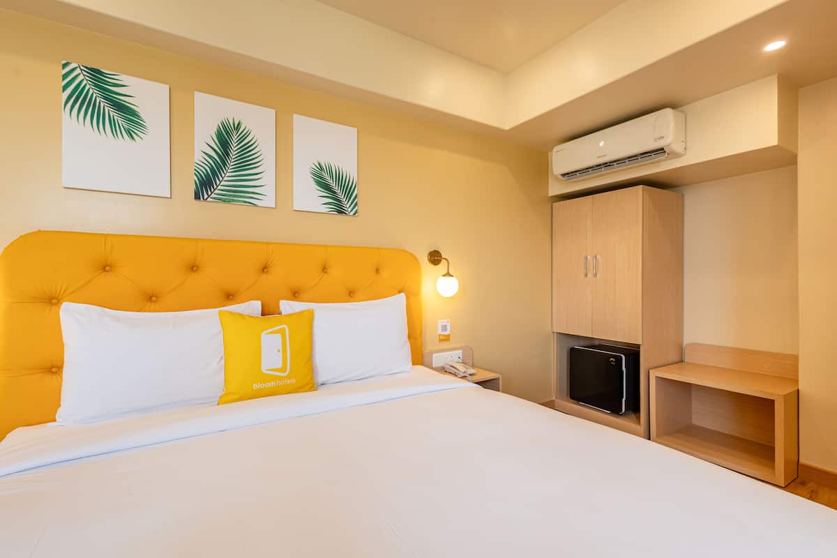 A hotel room with a large bed, a wooden wardrobe, and wall-mounted artwork.