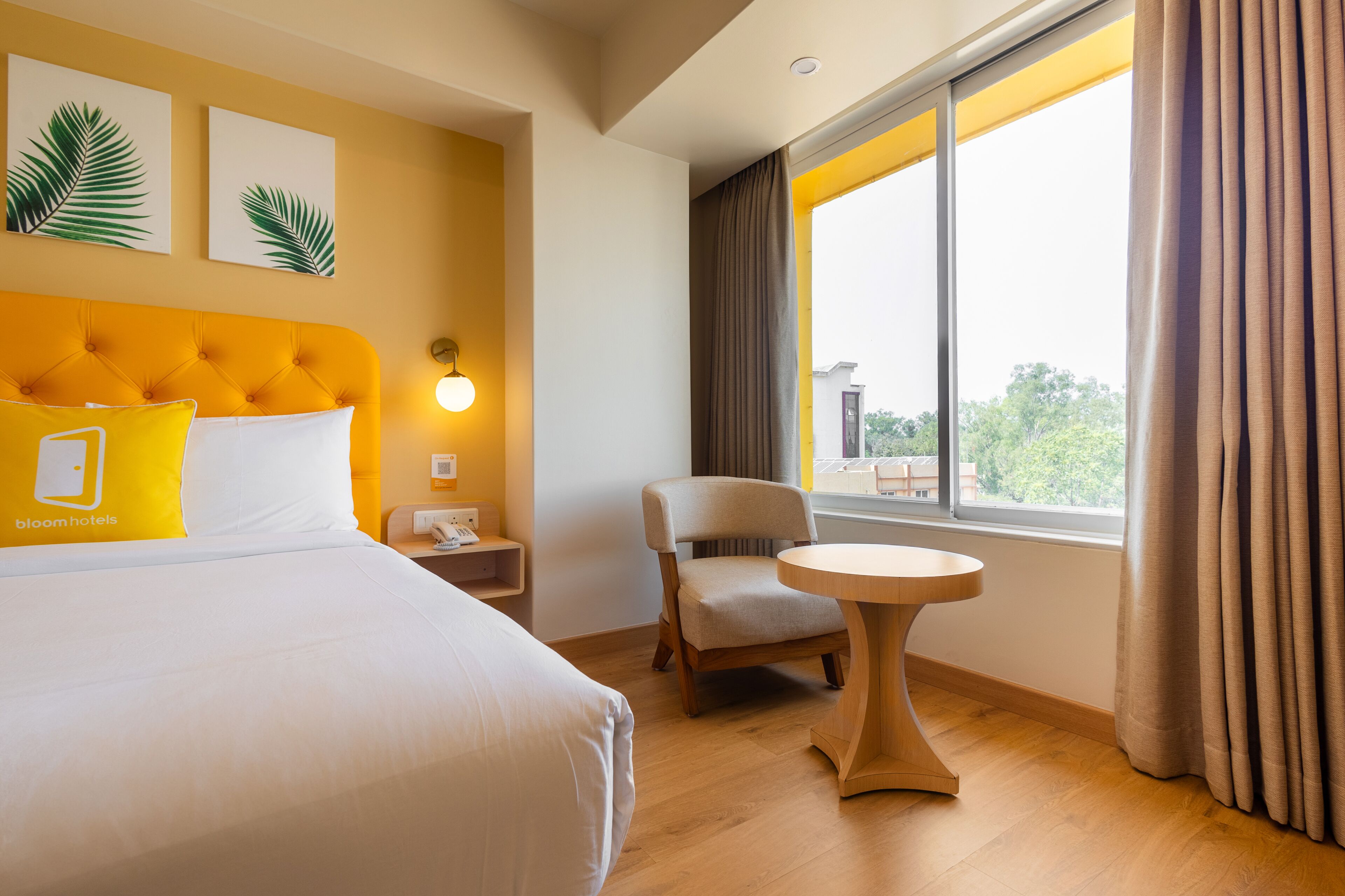 A hotel room with a bed, a chair, a small table, and a window with curtains.