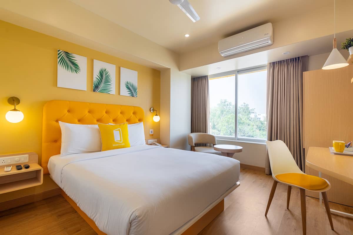 A hotel room with a large bed, a desk, a chair, and a window with curtains.