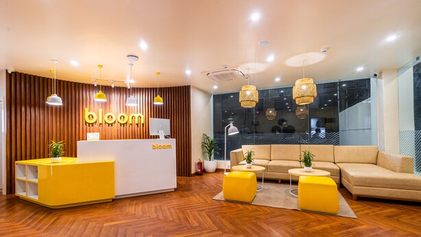 A modern reception area with a wooden panel wall, a reception desk, and a seating area with a sofa and ottoman. - Bloom Hotel - Ranchi (Ranchi)