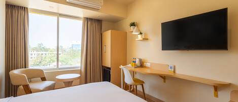 A hotel room with a large bed, a desk with a chair, a TV mounted on the wall, and a window with curtains.