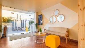 A modern interior with a wooden floor, a yellow ottoman, a beige sofa, and a round table with a lamp. - Bloom Hotel - Ranchi (Ranchi)