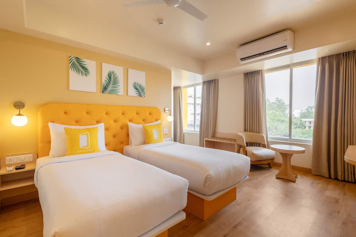 A hotel room with two beds, a chair, a small table, and a window with curtains.