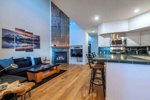 A modern living room with a fireplace, a dining area with bar stools, and a kitchen with stainless steel appliances. - Teton Homestead: Teton Timeout on Ski Hill Road (Driggs)
