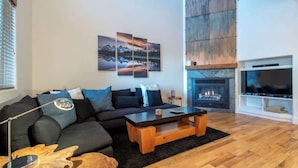 A modern living room with a dark-colored sofa, a wooden coffee table, and a fireplace. - Teton Homestead: Teton Timeout on Ski Hill Road (Driggs)