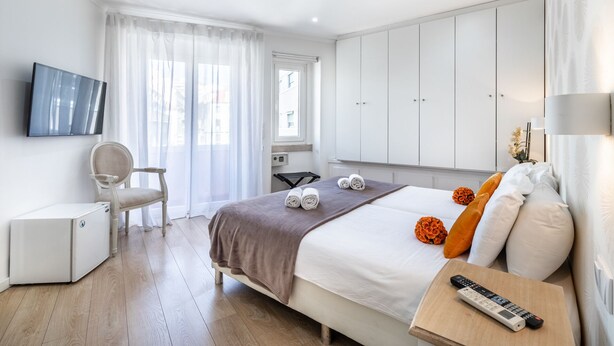 A hotel room with a bed, a desk, a chair, a TV, and a wardrobe. - Lisbon Terrace Suites for Large Groups (Lisbon)