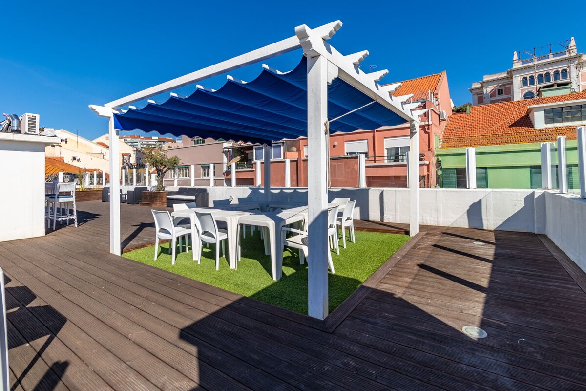 A rooftop patio with white chairs and tables, a blue awning, and a wooden deck.