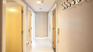 Un couloir avec des portes en bois, un porte-manteau et un interrupteur sur le mur.