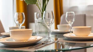 Une table à manger dressée avec de l’assiette blanche, des bols et de la verrerie transparente, agrémentée d’un vase de fleurs.