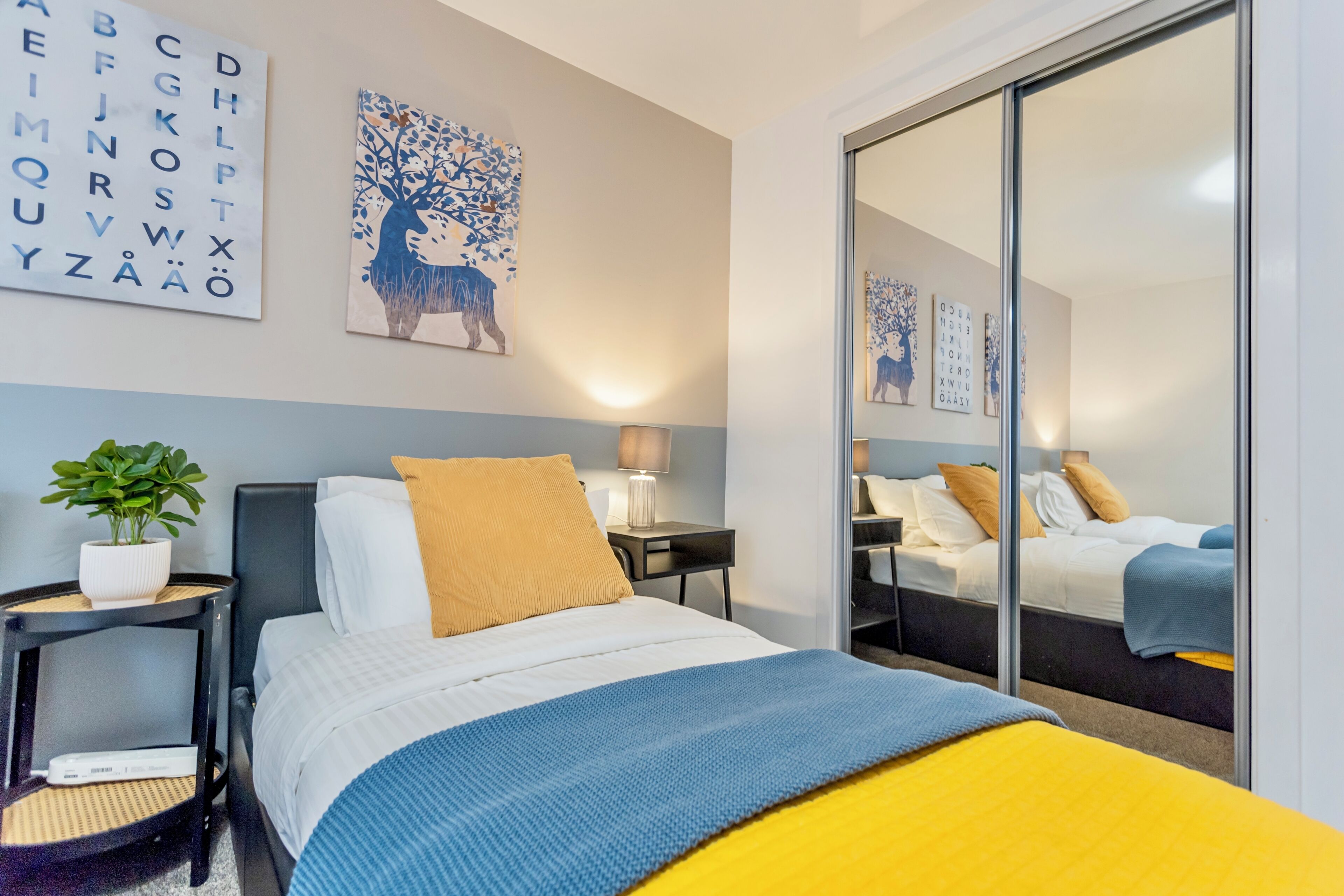 A hotel room with a bed, a nightstand, a lamp, a mirror, and a wall with alphabet art.