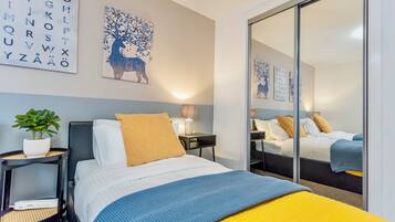 A hotel room with a bed, a nightstand, a lamp, a mirror, and a wall with alphabet art.
