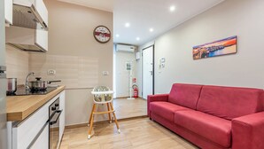 A modern kitchen with a stove, oven, and a high chair. A red sofa is in the living area, and a painting is on the wall. - Levante Home in the Centre of Bari (Bari)