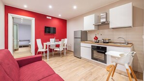 A modern kitchen with white cabinets, a built-in oven, and a stainless steel refrigerator. There is a dining area with a table and chairs, and a red wall with a mounted TV. - Levante Home in the Centre of Bari (Bari)