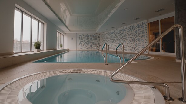 A large indoor swimming pool with a hot tub in the foreground, surrounded by windows and a decorative wall. - Waterlane Island Gdańsk Apartment 15 (Sopot)