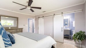 Un dormitorio con cama, ventilador de techo, armario corredero, baño con lavabo e inodoro, y una planta en maceta.
